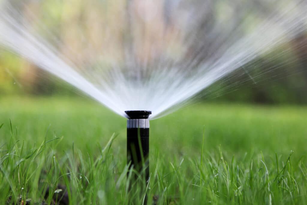 Un arroseur automatique arrosant une pelouse avec un jet d'eau en éventail.