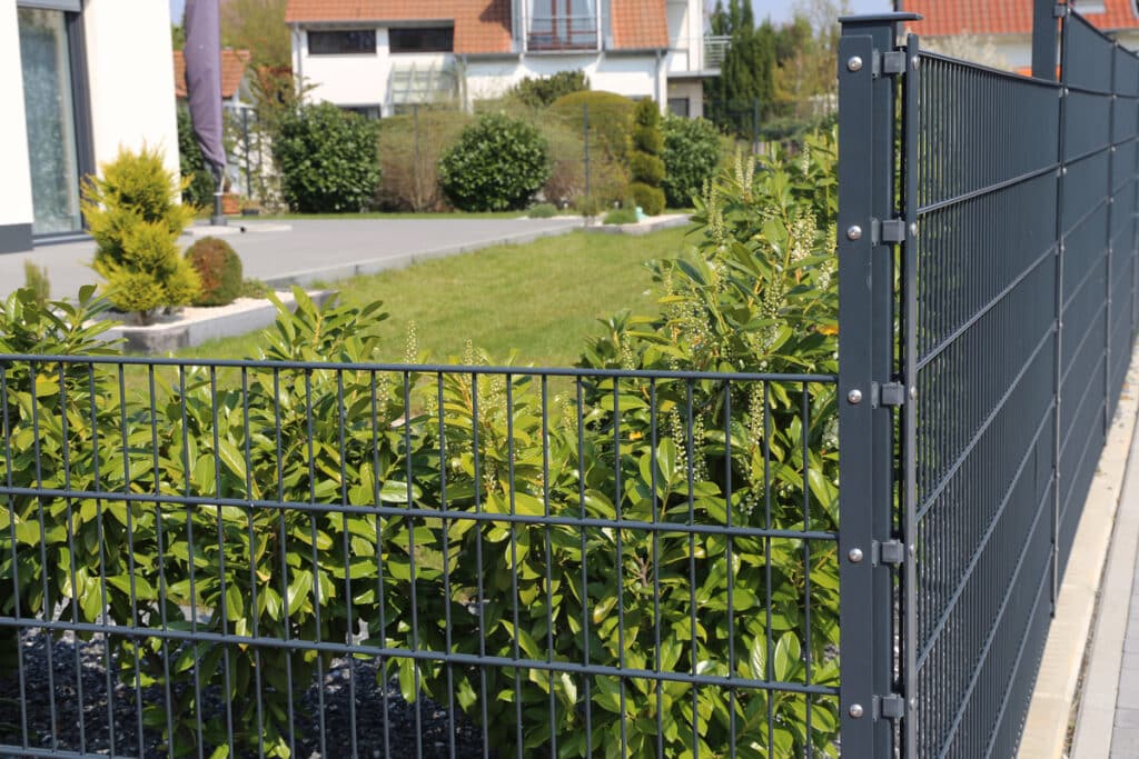 Clôture Métal Double Fil - Design Jardin Moderne Clôture métallique gris foncé à double fil bordant un jardin avec buissons verts fleuris et pelouse.