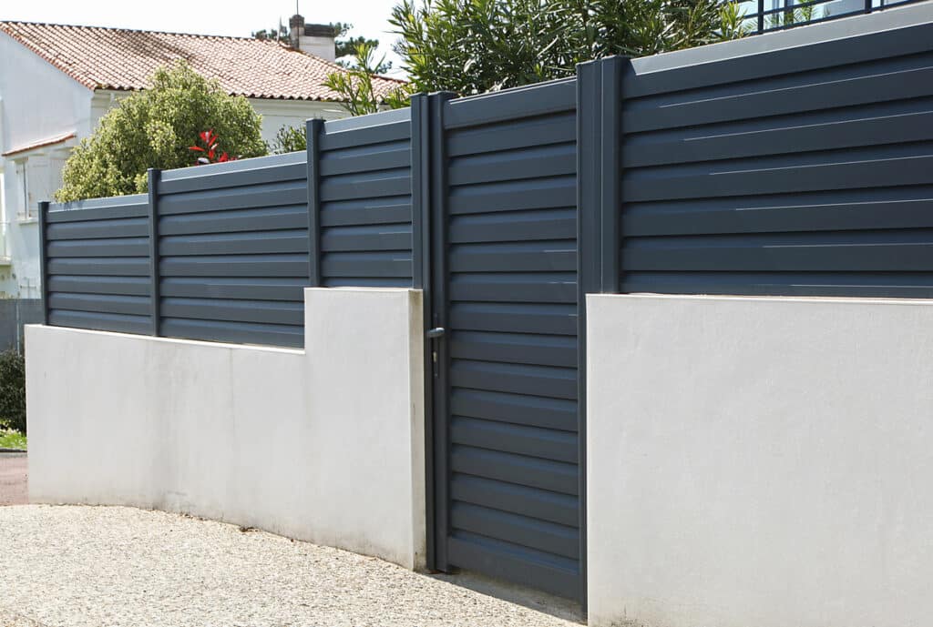 Clôture et portail gris foncé en aluminium sur un mur bas blanc. Ensemble moderne pour l'entrée de jardin.